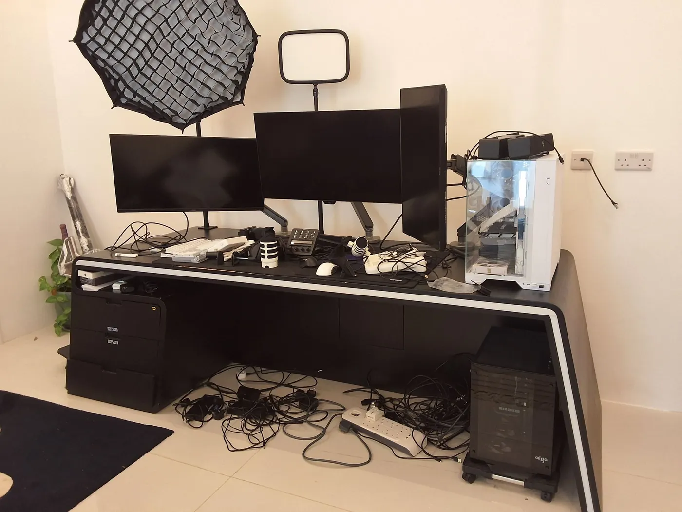 Triple-monitor creator desk: the cable nest gone from the floor, the tower lit — before